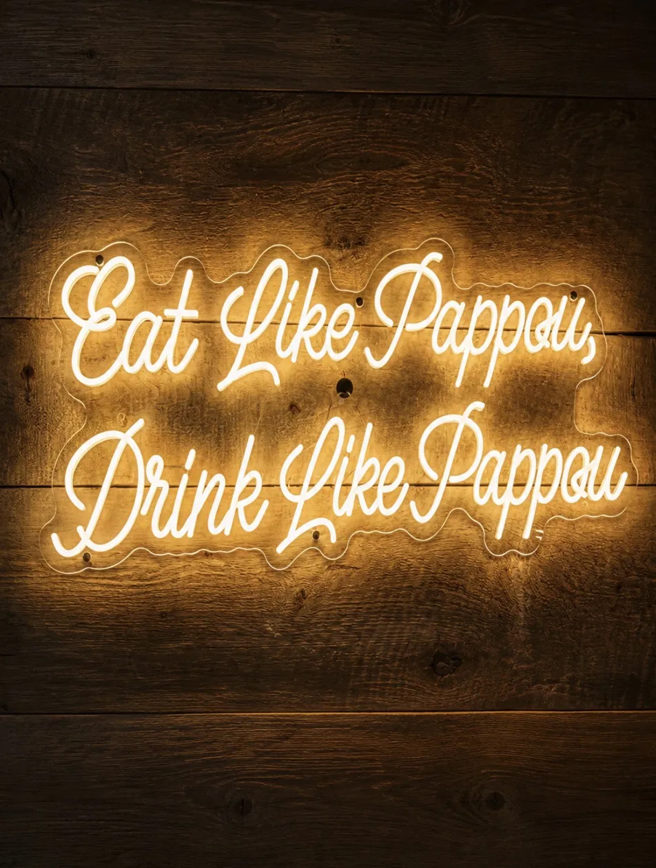 Neon sign reading 'Eat Like Pappou, Drink Like Pappou' glowing on warm wood